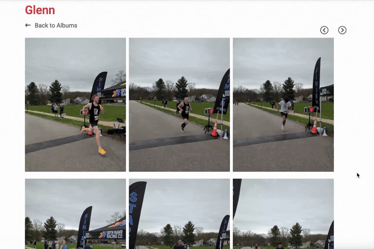A photo album page titled ‘Glenn’ (name shown at top left in red). A ‘Back to Albums’ link appears beneath the title. The main content is a grid of race photos at a finish line on an overcast day. In the top row, three large images show runners crossing a timing mat near a tall black FINISH flag/banner and orange cones; a few spectators and other runners are visible in the background along a road with grassy areas and trees. At the top right are circular left/right navigation arrows. The lower row shows additional race images partially visible.